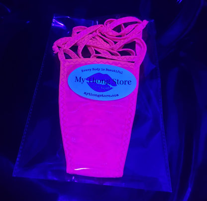 Black light reflective photo of Bright pink thong with side bows in brand package.