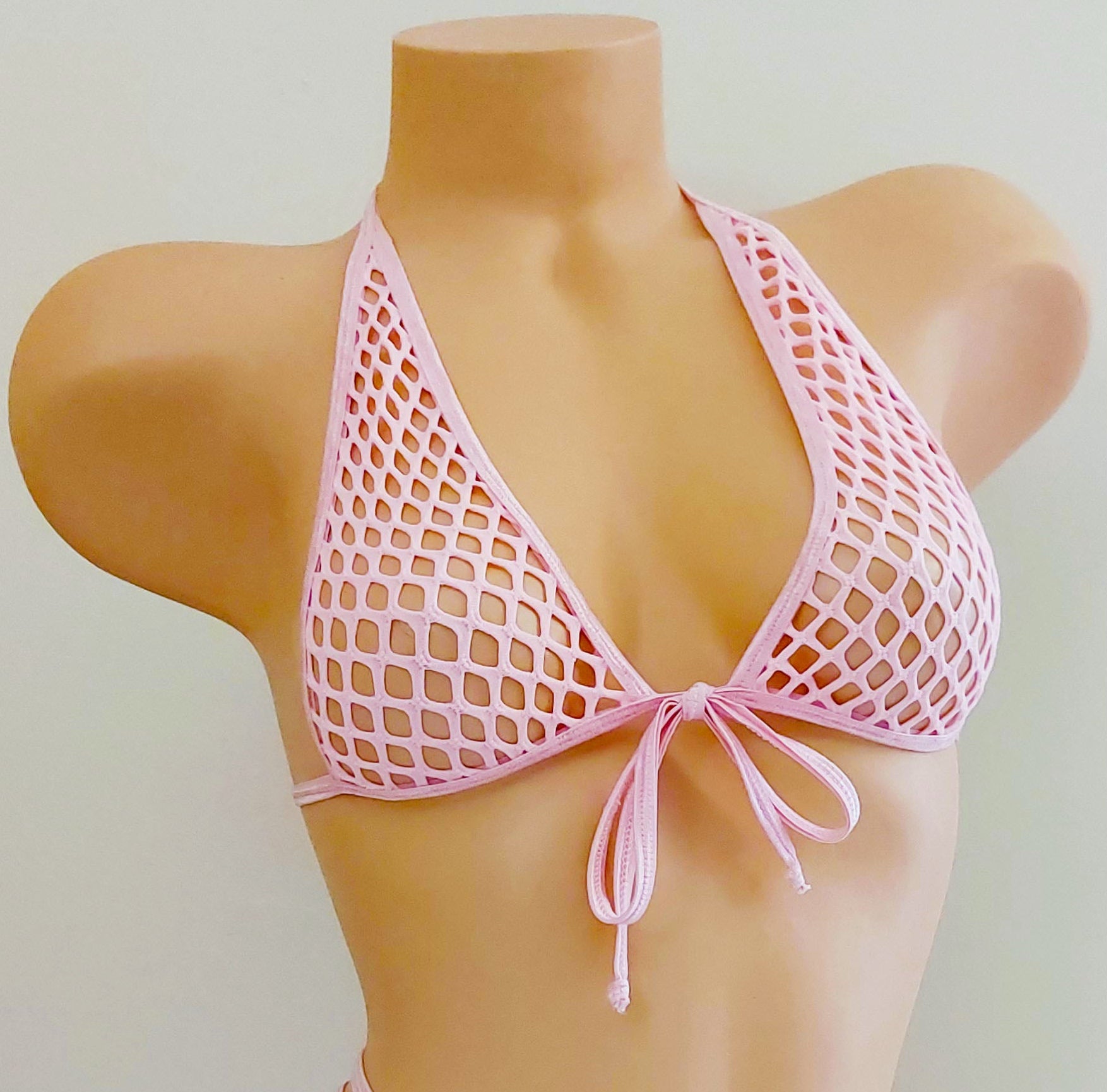 A pink fishnet string bikini set displayed on a tan mannequin torso against a plain light background.