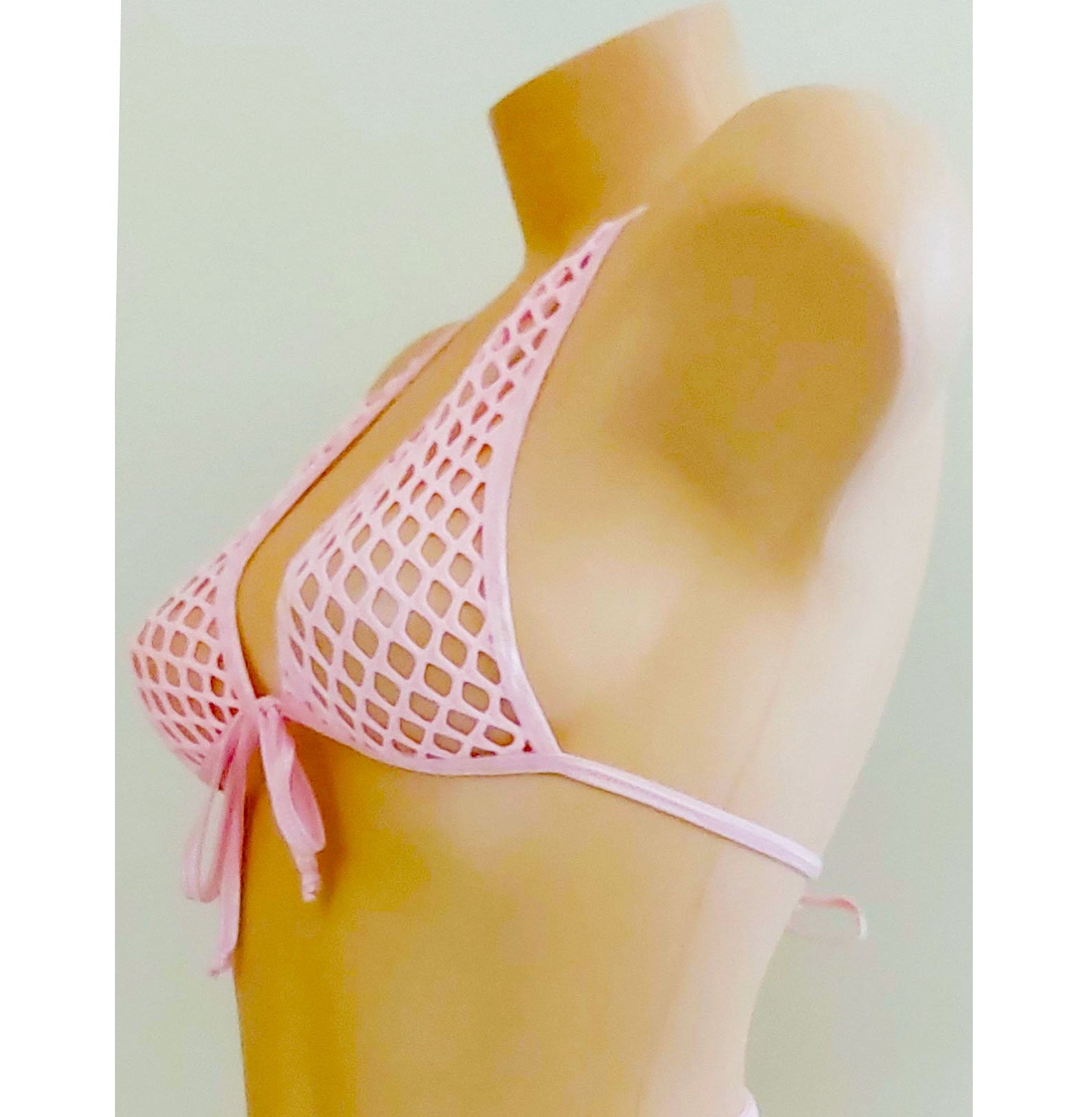 A pink fishnet bikini set displayed on a tan mannequin torso against a plain light background. The bikini features a halter top with side ties and matching strappy bottoms.