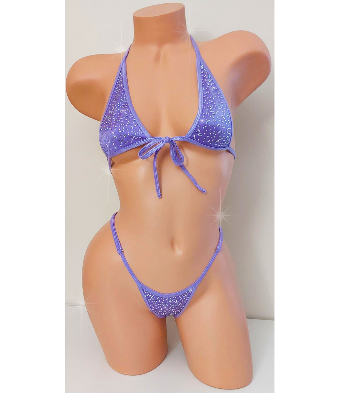 A two-piece bikini set in lavender purple with a glittery texture, displayed on a peach-colored mannequin torso. The bikini features a halter-style top with a front tie and matching low-rise bottoms.