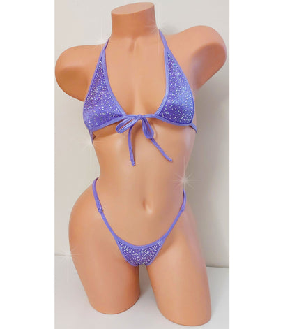 A two-piece bikini set in lavender purple with a glittery texture, displayed on a peach-colored mannequin torso. The bikini features a halter-style top with a front tie and matching low-rise bottoms.