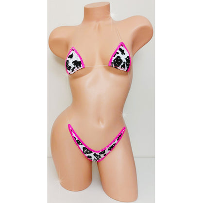A two-piece bikini set displayed on a beige mannequin torso. The bikini features a black and white cow print pattern with bright hot pink trim and matching pink straps.
