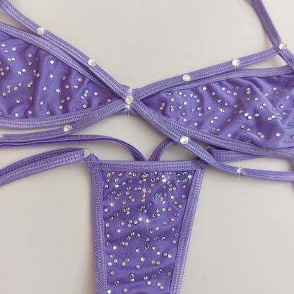 Purple strappy bikini top and thong set embellished with rhinestones, laid flat on a light beige background.